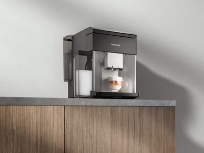 En helautomatisk espressomaskin EQ500 med en integrerad mjölkbehållare på en köksbänk. Det står en färdig cappuccino under utloppsröret