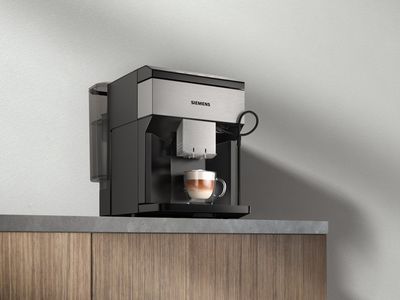 Fully automatic espresso machine EQ500 stands on a working top. There is a finished Cappuccino under the coffee spout