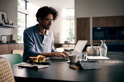Ein Mann sitzt am Küchentisch und schaut in seinen Laptop