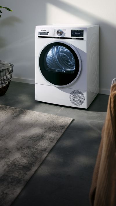 Siemens Wärmepumpentrockner in einem Raum für die Wäschepflege mit Pflanze und Wäscheständer.