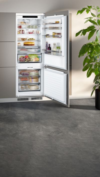 Ein mit Lebensmitteln gefüllter Siemens Einbau-Kühl-Gefrierschrank mit geöffneter Tür in einer modernen Küche. 