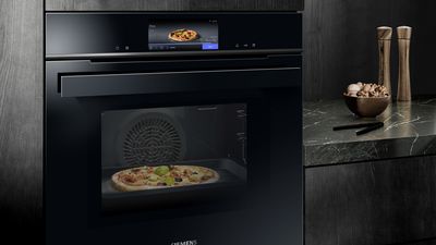 Un elegante forno nero con una pizza visibile all'interno, che mostra un pannello di controllo digitale sopra, sullo sfondo scuro della cucina.