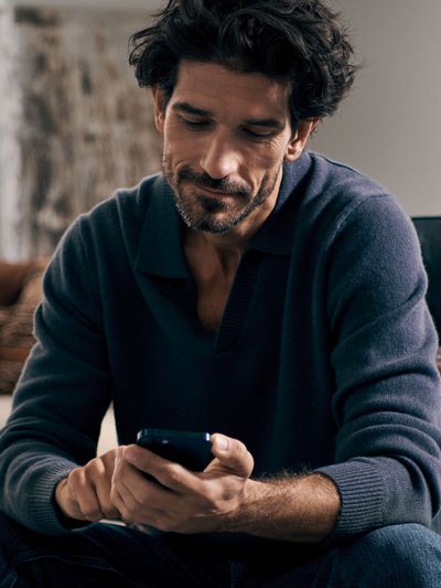 Un uomo è seduto comodamente in un soggiorno moderno e utilizza il suo smartphone