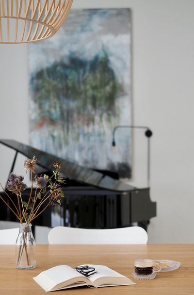 En kopp espresso og en åpen bok på bord foran et piano og stort maleri.