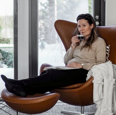 Heidi Lahti sitter i sin Arne Jacobsen lenestol Egget (Egg chair) og drikker en god kopp kaffe.