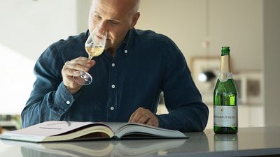 Smakexperten Richard Juhlin provar ett glas med sitt mousserande vin. Framför honom ligger en stor bok om vin.