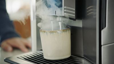Rykende varm melke fra espressomaskin i kaffekopp