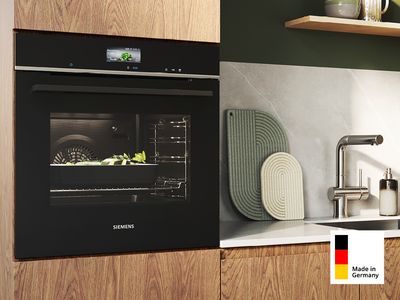 Ein Siemens Made in Germany Einbaubackofen in einer modernen Einbauküche aus Holz, integriert auf Augenhöhe neben einer Spüle.