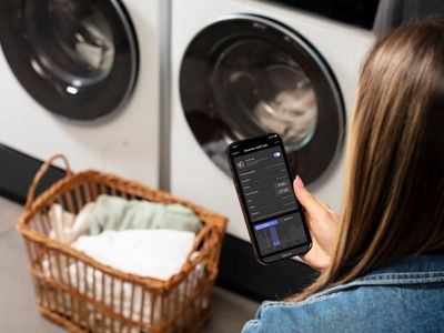 HomeWizard-app op smartphone met Siemens wasmachine en droger op de achtergrond