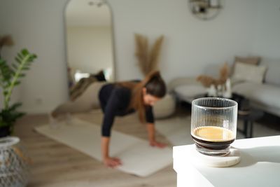 À l'arrière-plan, Lisa, amatrice de café, fait une planche sur le tapis de yoga de son salon. À l'avant, un verre rempli d'expresso fraîchement préparé. C'est ainsi qu'elle associe café et santé mentale.