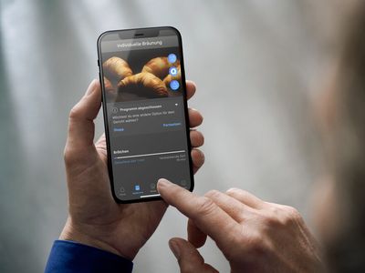 Backofen mit Kamera im Inneren. Ein Smartphone zeigt die Kameraaufnahme von Innen. Im Backofeninneren befinden sich gebräunte Croissants.