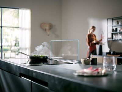 Siemens Induktionskochfeld mit einem Kochfeld-Dunstabzug glassdraftAir, der bei Bedarf hinter dem Kochfeld herausgefahren werden kann. Auf dem Kochfeld steht eine Pfanne mit Gemüse.