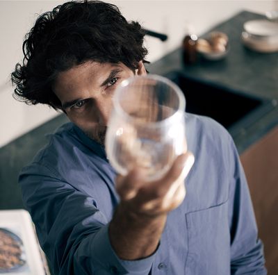 Alt Text: Ein Mann hält ein Weinglas nach oben und prüft die Sauberkeit des Glases. Daneben sieht man einen geöffneten Siemens Geschirrspüler