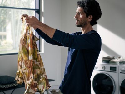 Osoba trzyma kolorowy, wzorzysty szalik w dobrze oświetlonej pralni, w otoczeniu pralek i miękkich mebli.