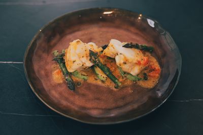 Auf einem Teller angerichtetes gedämpftes Fischfilet mit grünem Spargel und Soße.