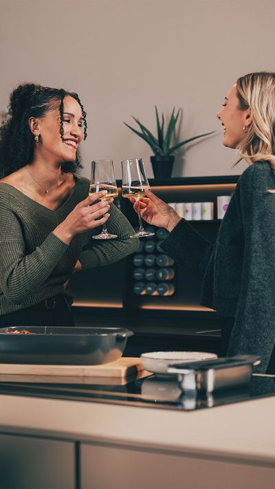 Zwei Frauen stoßen mit Weingläsern in einer modernen Küche mit Siemens Geräten an.