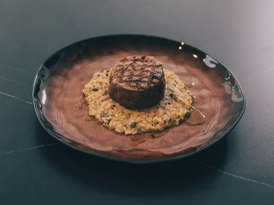 Rinderfilet auf cremigem Waldpilzrisotto auf einem braunen Teller.
