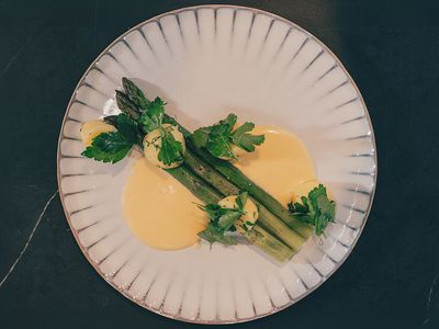Grüner Spargel mit Sauce Hollandaise und Kartoffeln auf einem weißen Teller.