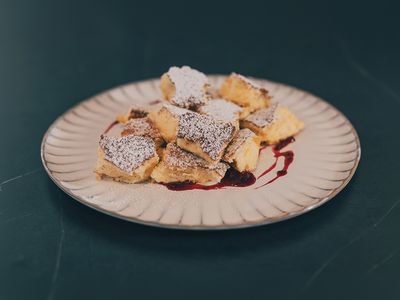 Rahmschmarren auf weißem Teller, bestreut mit Puderzucker, serviert mit Beerensauce.