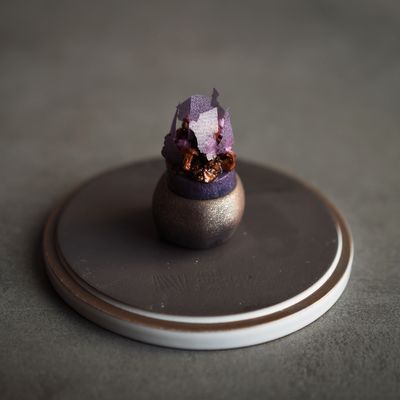 Un dessert gourmand composé d'une base sphérique aux accents violets et dorés, surmontée de délicats éclats violets texturés.