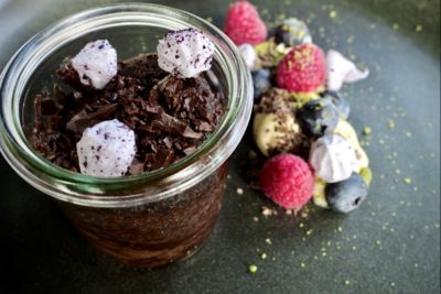 Glasskrukke med sjokoladedessert, toppet med pisket krem og friske bringebær, omgitt av spredte bær.