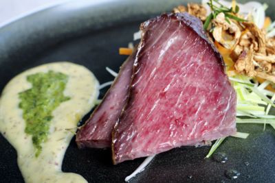 Stekt biff med grønn saus, grønnsaker og nudler på en svart tallerken.