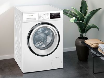Siemens-pesukone avonaisella ovella, modernissa ympäristössä ja viherkasvin vieressä. 