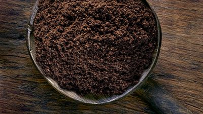 Een close-up van boven van een kom gemalen koffie op een donkere houten tafel.