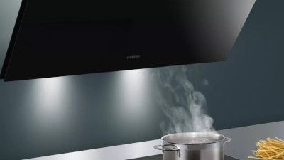 Un'elegante cappa da cucina nera sopra una pentola su un moderno piano cottura illuminata da una soffusa luce sotto il mobile.