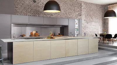 Cucina moderna con armadietti grigi, grande isola in legno chiaro, con parete in pietra e zona pranzo sullo sfondo.
