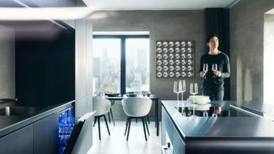 Un uomo si trova in una cucina moderna ed elegante con in mano due bicchieri da vino.