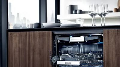 Aperta lavastoviglie con piatti puliti, bicchieri e elettrodomestici da cucina in moderno interno cucina.