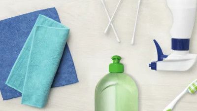 Un'immagine piatta di articoli per la pulizia: due panni, un flacone spray, un sapone liquido, su uno sfondo chiaro.
