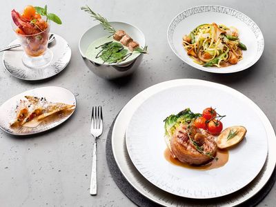 Une table avec des plats préparés, dont une salade dans un verre, des pâtes, une soupe, une assiette de viande et de légumes rôtis, et une tranche de pâtisserie pour le dessert.