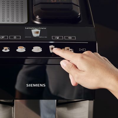 Een close-up van iemand die met zijn vinger op het latte-symbool op een volautomatische espressomachine van Siemens drukt