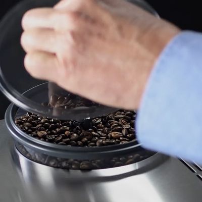 Een close-up van iemands hand die het deksel van het bonenreservoir optilt op een volautomatische espressomachine van Siemens.