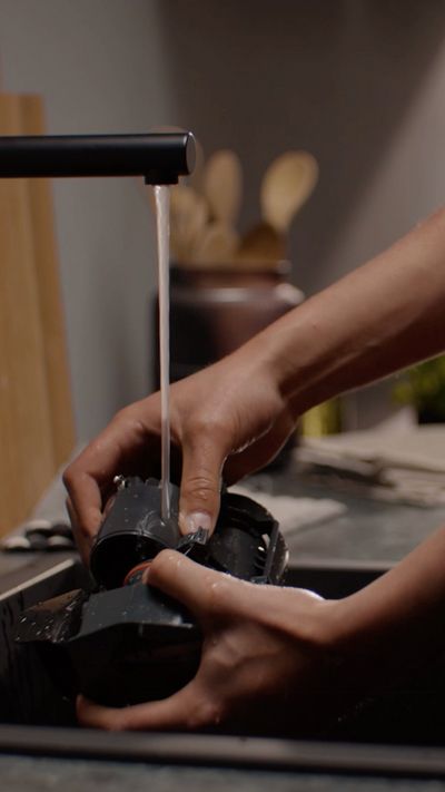 Personne rinçant les composants d'une machine à café sous un robinet noir moderne dans un évier de cuisine.