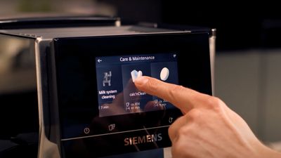 Un doigt effleurant l'écran tactile d'une machine à café Siemens, sélectionnant le programme calc'nClean dans la section Entretien & Maintenance du menu.