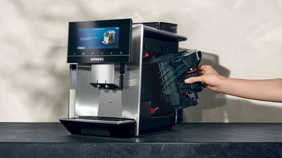 La main d'une personne retirant l'unité de percolation du côté droit d'une machine à café automatique Siemens.