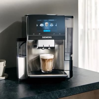 Machine à café EQ700 servant un verre de café latte, posée sur un plan de travail en marbre noir.