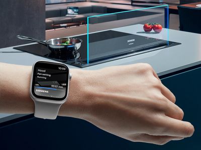 A hand holds an Apple Watch, positioned in front of a stylish kitchen, highlighting the blend of technology and home life.