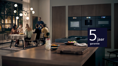 Moderne keuken met eethoek, mensen die werken op laptops, keukenapparatuur, en 5 jaar garantieteken.
