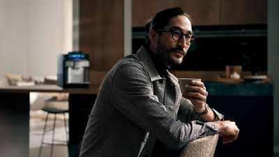 Un homme en chemise à carreaux assis avec une tasse dans une cuisine moderne.