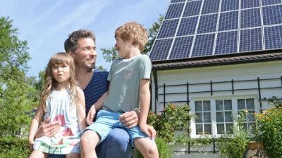 Famiglia di tre seduti davanti a pannelli solari su una casa, godendo l'esterno.