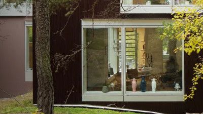 Una casa moderna con grandi finestre in vetro che mostrano vasi decorativi, circondata da verde e alberi.