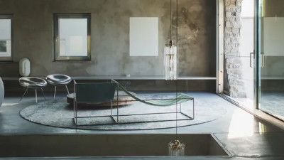 Interno moderno con mobili minimalisti, tra cui una chaise longue elegante, due sedie e un tappeto circolare.