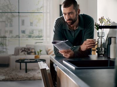 Un uomo consulta il manuale di un apparecchio, appoggiato al piano della cucina sotto cui si trova una lavastoviglie da incasso con lo sportello socchiuso.