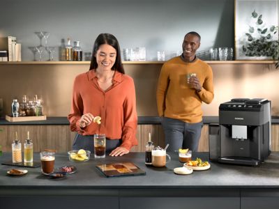 Un homme et une femme dégustant des boissons au café dans une cuisine moderne avec une machine à café automatique Siemens sur le comptoir.