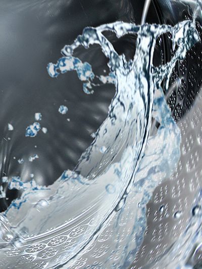 &Eacute;claboussures d'eau &agrave; l'int&eacute;rieur d'un tambour de lave-linge chrom&eacute; propre et immacul&eacute;.