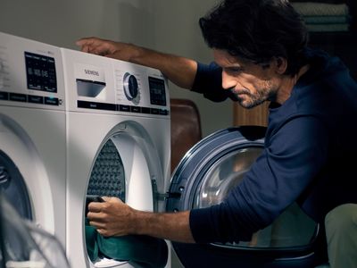 Ein Mann bel&auml;dt seinen Trockner, w&auml;hrend ihm die Sonne durch das Fenster ins Gesicht scheint.